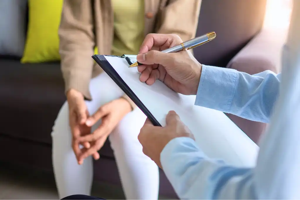 Close-up of a mental health professional taking notes during a therapy session with a seated patient.