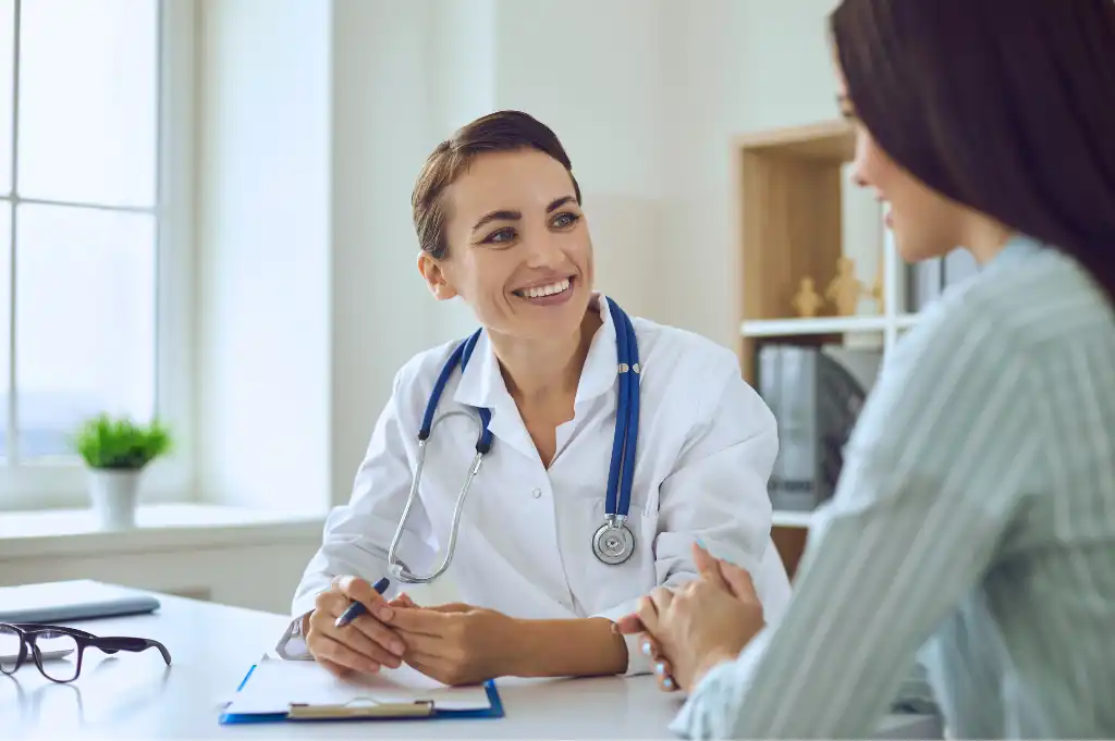 Smiling female doctor with stethoscope talking to a female patient in a bright medical office.
